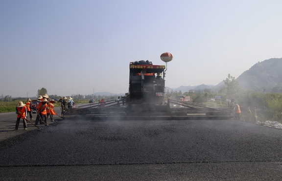 2019年8月，宜春經(jīng)開區(qū)S311路面攤鋪現(xiàn)場，工友們輔助路面兩側(cè)的分料、補(bǔ)窩等作業(yè)